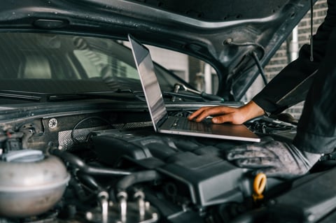 A mechanic using a laptop on a car engine for diagnostics