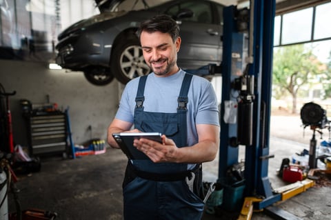 Smiling mechanic using a digital tablet next to a car on a hydraulic lift